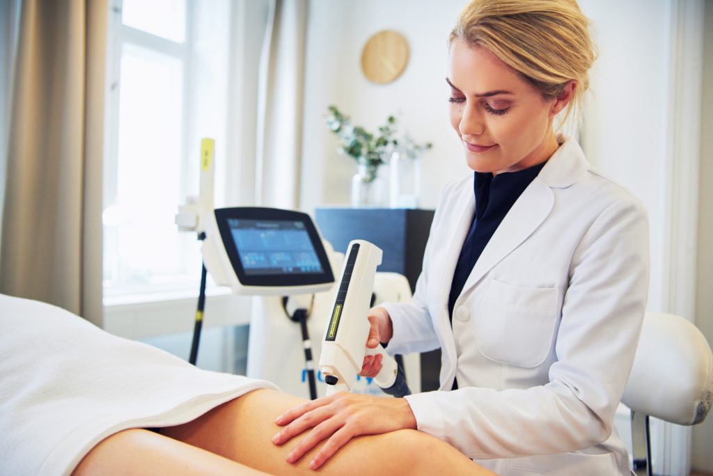 Clinic technician performing electrolysis on a female client's leg